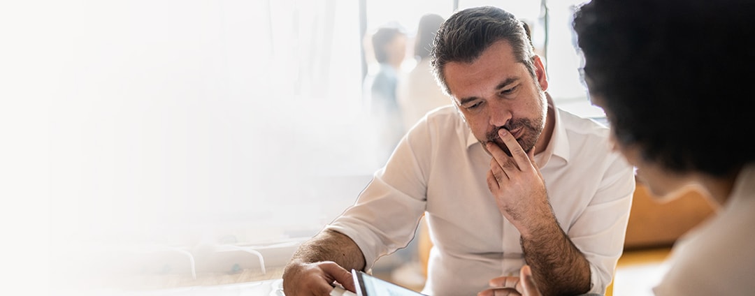 Client and advisor sitting at a table, discussing financial strategies using a digital tablet.
