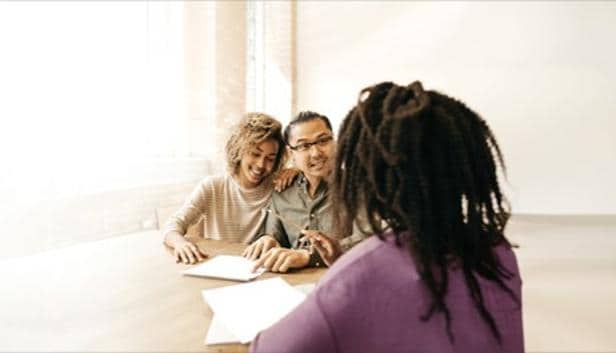 Financial advisor meeting with two clients at a table, reviewing documents in a bright office setting.