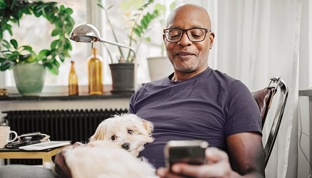 A man sits with a dog on his lap, appearing content as he looks down at his cell phone.