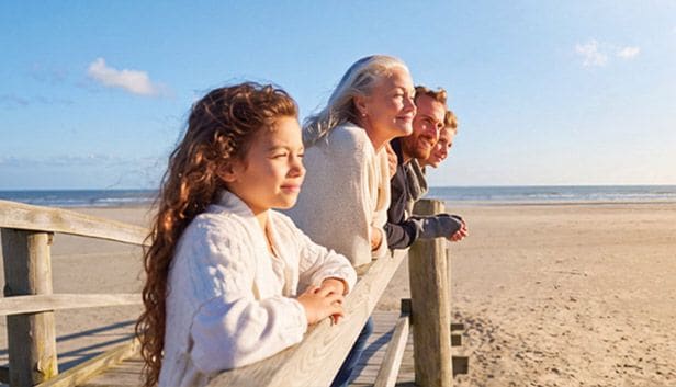 Lifestyle. Family members leaning on a beachside railing and looking toward the ocean.