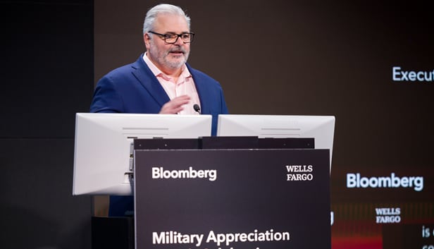 Wells Fargo and Bloomberg logos behind panelists with Military Appreciation signage in front of speaker